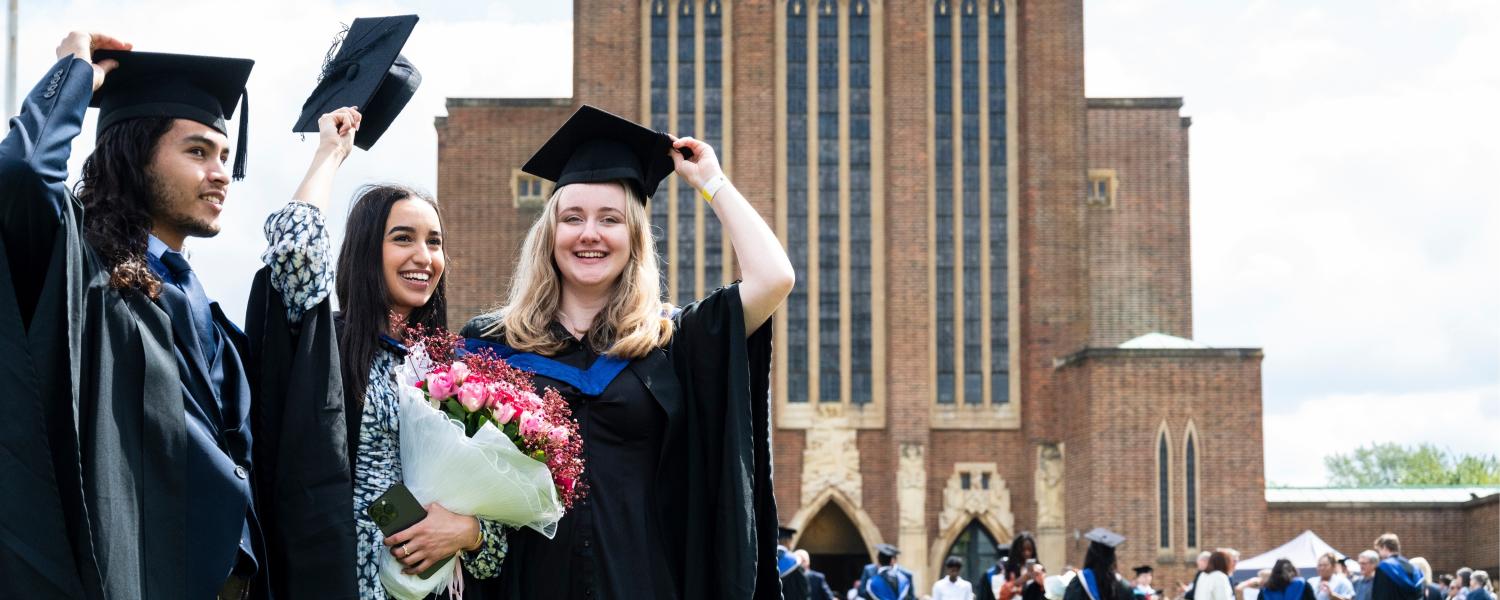 Three students in graduation robes and hats outside the cathedral