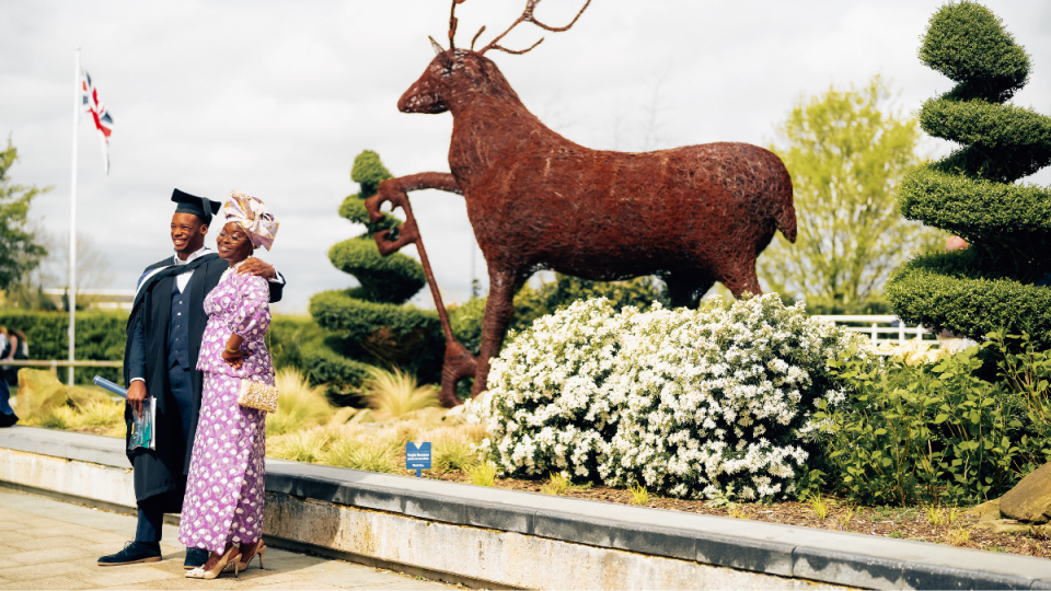 A graduand having a photo taken with their guest by the stag statue 